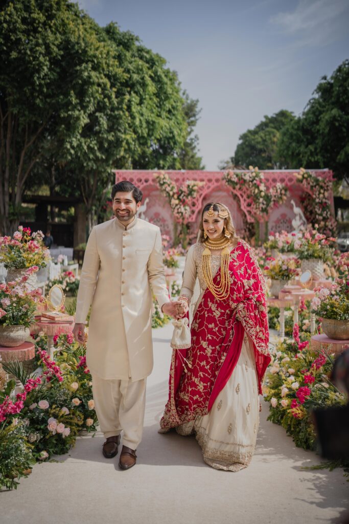Luxury Pakistani wedding couple portrait walking through floral entrance, documentary style wedding photography in Pakistan, Dubai, UK & USA